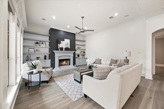 living room with light wood-type flooring, ceiling fan, built in shelves, and a fireplace