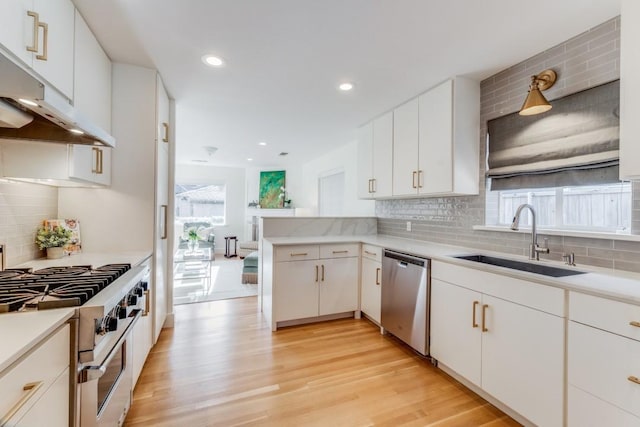 kitchen with sink, white cabinetry, light hardwood / wood-style floors, kitchen peninsula, and appliances with stainless steel finishes