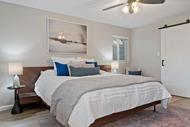 bedroom featuring hardwood / wood-style flooring, ceiling fan, and a barn door