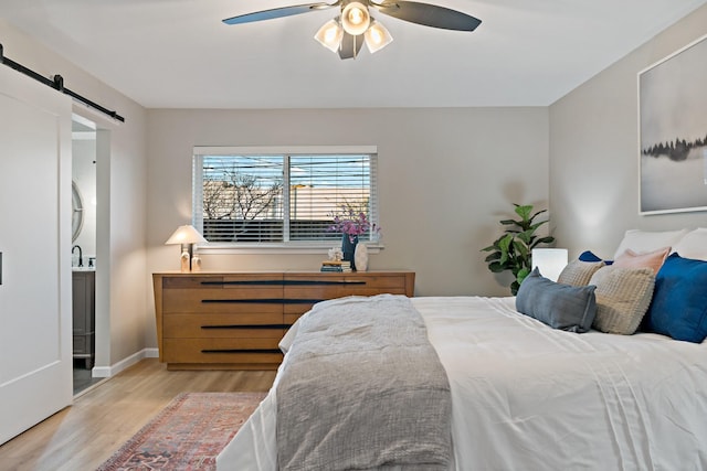 bedroom featuring sink, light hardwood / wood-style floors, a barn door, and ceiling fan