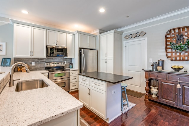 kitchen featuring stainless steel appliances, a kitchen island, backsplash, white cabinetry, and sink