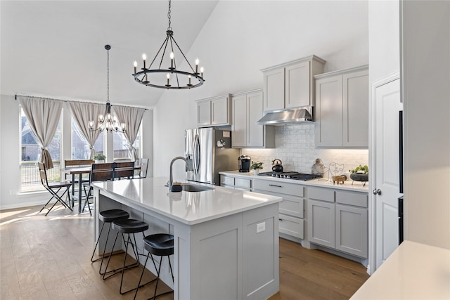 kitchen featuring decorative light fixtures, an island with sink, tasteful backsplash, light wood-type flooring, and appliances with stainless steel finishes