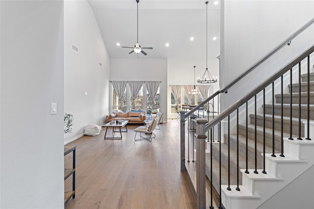 staircase with ceiling fan with notable chandelier, a towering ceiling, and hardwood / wood-style flooring