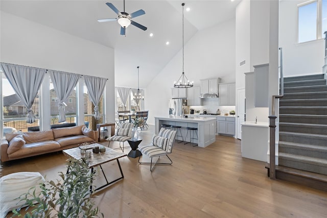 living room with light wood-type flooring, high vaulted ceiling, and ceiling fan with notable chandelier