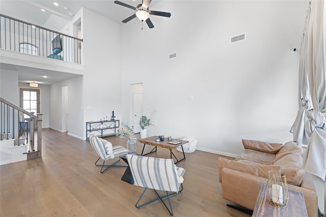 living room with a high ceiling, ceiling fan, and light wood-type flooring