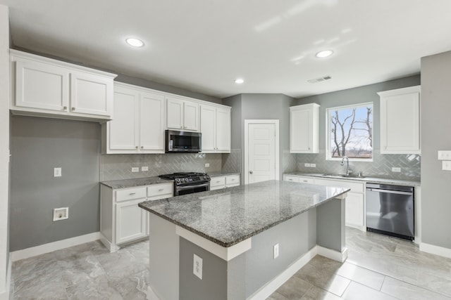 kitchen featuring stainless steel appliances, a center island, stone counters, white cabinets, and sink