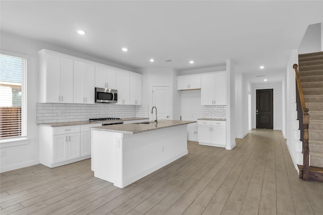 kitchen with sink, a center island with sink, white cabinetry, and tasteful backsplash