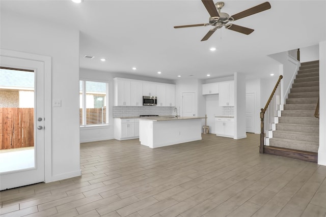 kitchen with a center island with sink, light wood-type flooring, backsplash, white cabinets, and ceiling fan