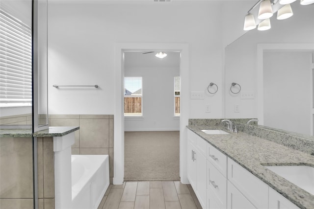 bathroom with ceiling fan, a tub to relax in, and vanity