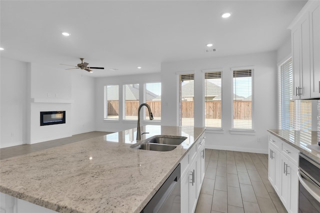 kitchen featuring light stone countertops, stainless steel appliances, a center island with sink, white cabinets, and sink