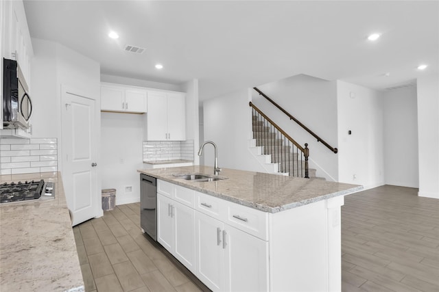 kitchen featuring sink, a center island with sink, white cabinetry, and light stone countertops