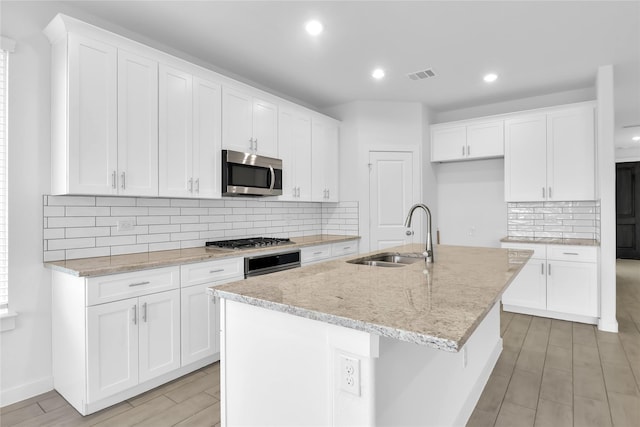 kitchen with a kitchen island with sink, stainless steel appliances, decorative backsplash, sink, and white cabinetry