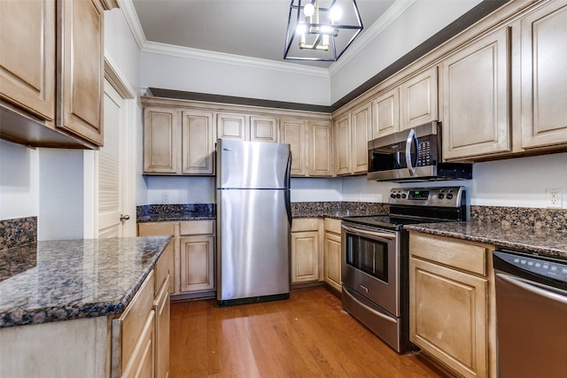 kitchen featuring dark stone countertops, hardwood / wood-style floors, ornamental molding, and appliances with stainless steel finishes