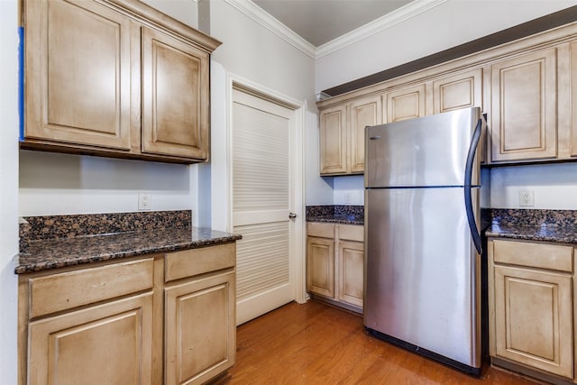 kitchen featuring stainless steel refrigerator, dark stone counters, ornamental molding, light brown cabinets, and light hardwood / wood-style flooring