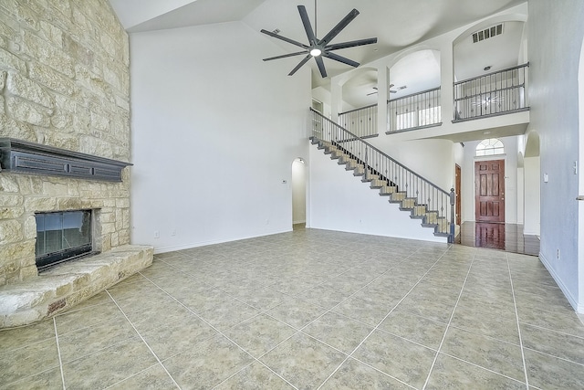 unfurnished living room featuring a towering ceiling, ceiling fan, tile patterned floors, and a stone fireplace