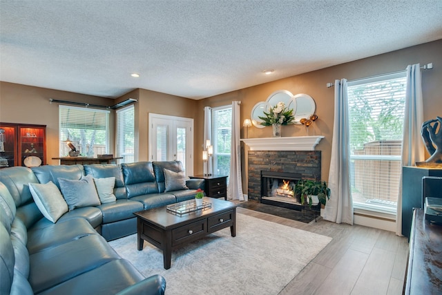 living room with french doors, a textured ceiling, light hardwood / wood-style floors, and a stone fireplace