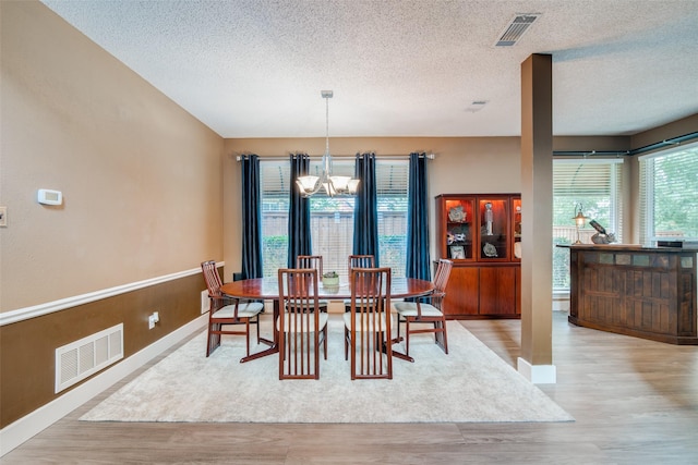 dining room with a textured ceiling, a notable chandelier, and light hardwood / wood-style flooring