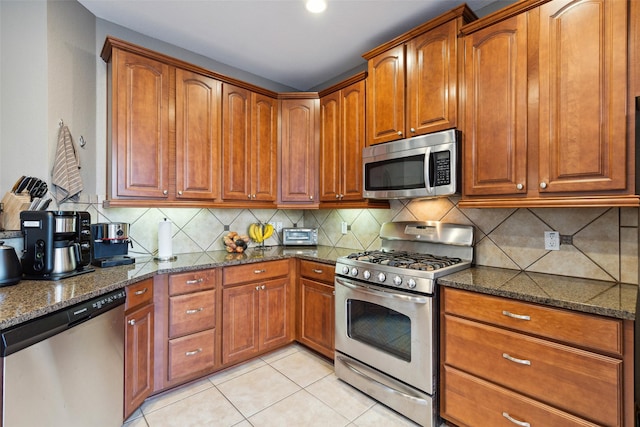 kitchen with appliances with stainless steel finishes, dark stone counters, decorative backsplash, and light tile patterned floors