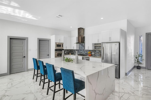 kitchen featuring a large island, wall chimney range hood, appliances with stainless steel finishes, white cabinetry, and light stone countertops