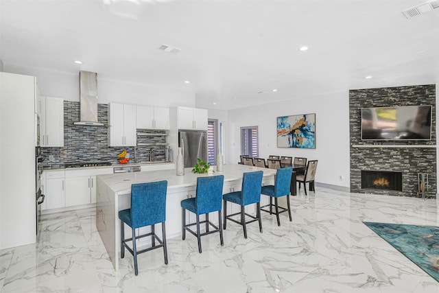 kitchen with wall chimney range hood, a breakfast bar area, appliances with stainless steel finishes, white cabinetry, and a center island