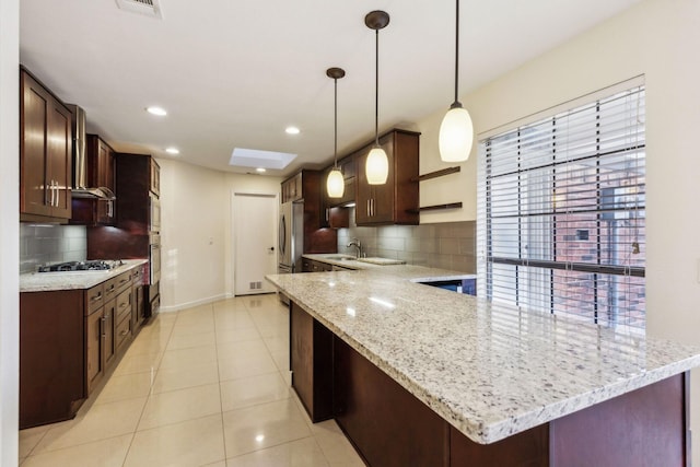 kitchen featuring hanging light fixtures, a skylight, kitchen peninsula, stainless steel fridge, and decorative backsplash