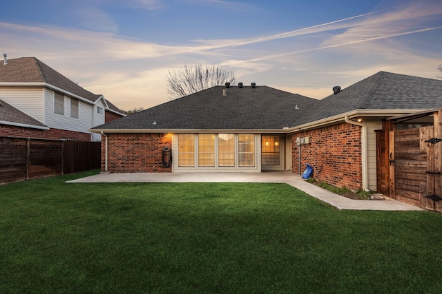 back house at dusk featuring a patio area and a yard