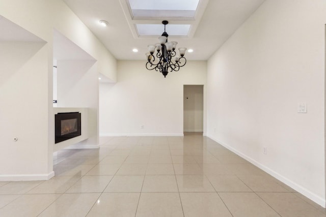 unfurnished living room with a multi sided fireplace, an inviting chandelier, a skylight, and light tile patterned floors