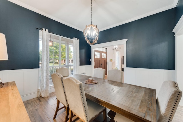 dining space with a wainscoted wall, light wood finished floors, crown molding, and a notable chandelier