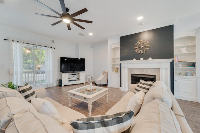 living area with built in features, visible vents, wood finished floors, crown molding, and a fireplace