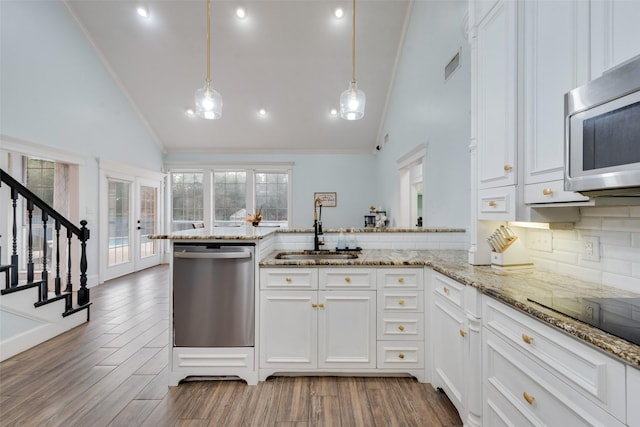 kitchen with stainless steel appliances, kitchen peninsula, sink, white cabinetry, and decorative light fixtures