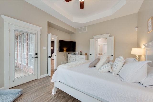 bedroom featuring access to outside, ceiling fan, a tray ceiling, and light hardwood / wood-style flooring