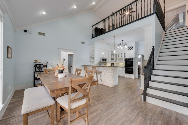 dining area featuring crown molding, visible vents, wood finished floors, high vaulted ceiling, and stairs