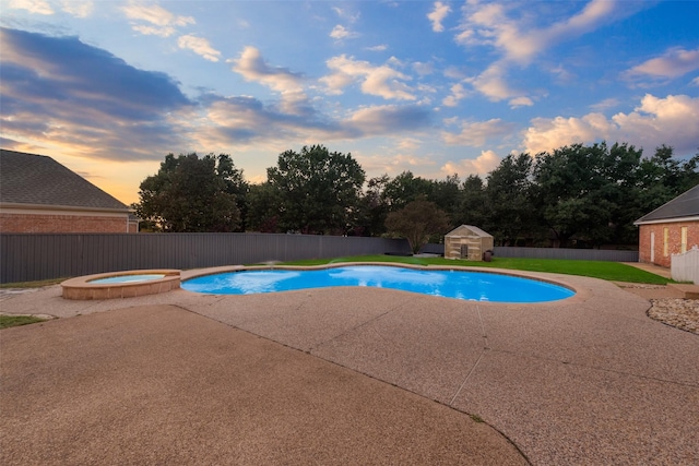 pool at dusk featuring a patio area, an in ground hot tub, and a storage shed