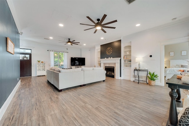 living room with a tile fireplace, ceiling fan, ornamental molding, light hardwood / wood-style flooring, and built in features