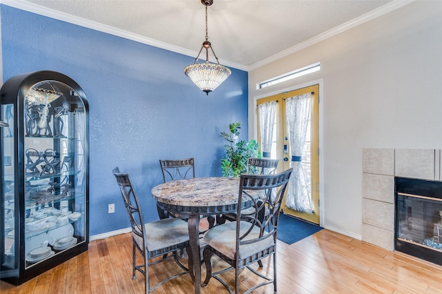 dining room with a textured ceiling, french doors, hardwood / wood-style floors, crown molding, and a tiled fireplace