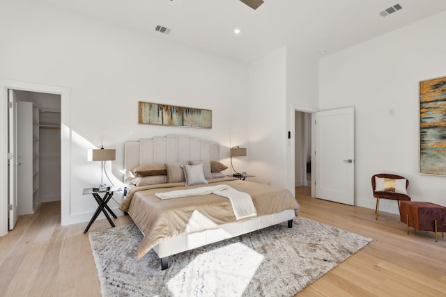 bedroom featuring a spacious closet, light hardwood / wood-style floors, a closet, and a towering ceiling