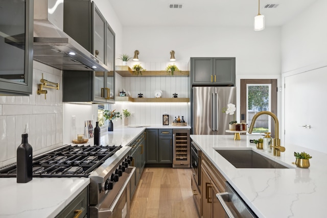 kitchen featuring premium appliances, decorative light fixtures, light stone countertops, wall chimney exhaust hood, and sink