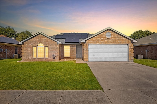 ranch-style house with solar panels, central air condition unit, a lawn, and a garage