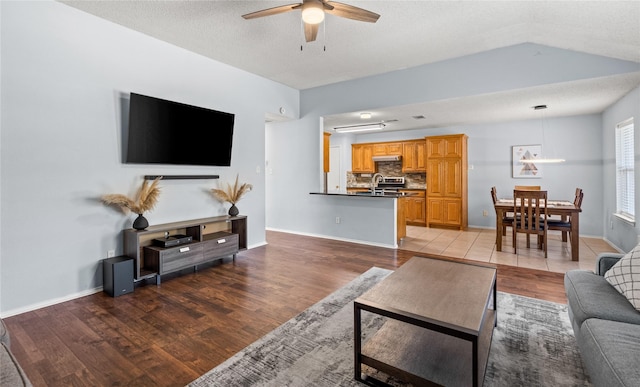 living room featuring sink, a textured ceiling, lofted ceiling, ceiling fan, and light hardwood / wood-style flooring