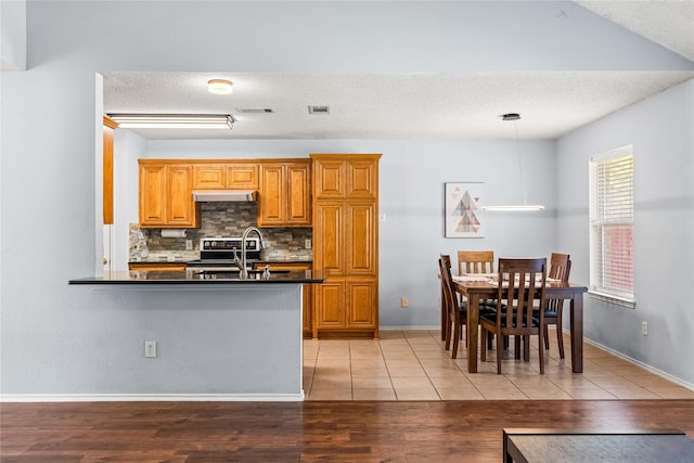 kitchen with kitchen peninsula, decorative light fixtures, decorative backsplash, stainless steel electric range, and sink