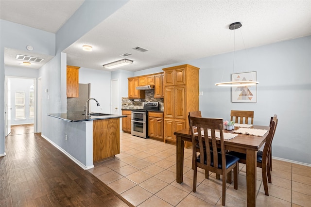 kitchen featuring kitchen peninsula, range with two ovens, decorative light fixtures, decorative backsplash, and sink