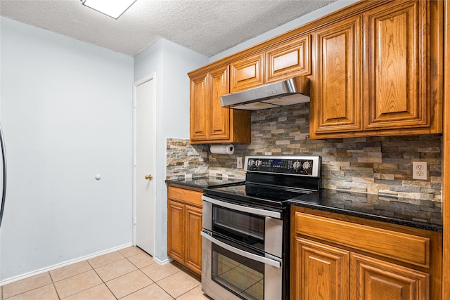 kitchen with dark stone countertops, light tile patterned floors, range with two ovens, a textured ceiling, and backsplash