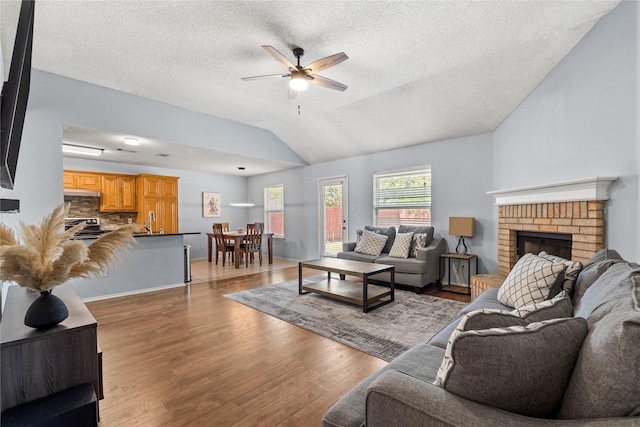 living room featuring a textured ceiling, vaulted ceiling, ceiling fan, wood-type flooring, and a brick fireplace