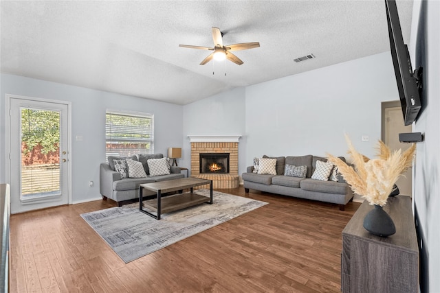 living room with a textured ceiling, lofted ceiling, ceiling fan, a brick fireplace, and dark wood-type flooring