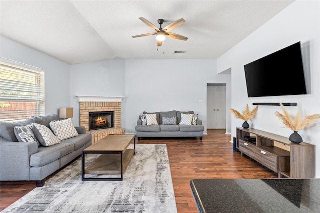 living room with vaulted ceiling, ceiling fan, dark wood-type flooring, a brick fireplace, and a textured ceiling