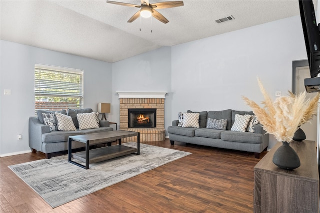 living room with a textured ceiling, vaulted ceiling, dark hardwood / wood-style floors, a brick fireplace, and ceiling fan