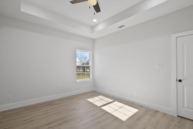 empty room with ceiling fan, a tray ceiling, and light hardwood / wood-style flooring