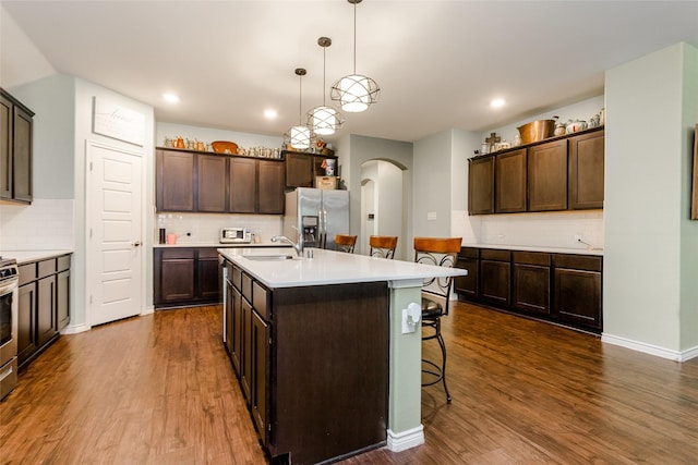 kitchen with pendant lighting, dark hardwood / wood-style flooring, an island with sink, stainless steel appliances, and dark brown cabinets