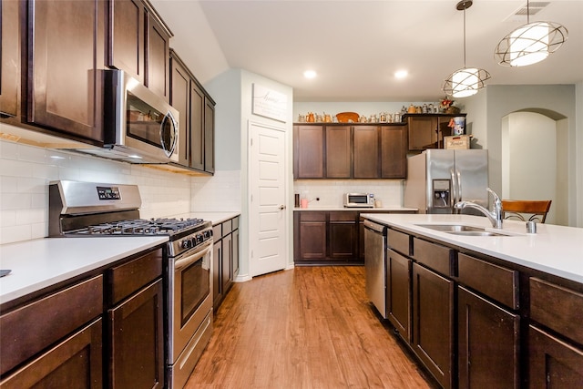 kitchen with stainless steel appliances, decorative light fixtures, light wood-type flooring, dark brown cabinets, and sink