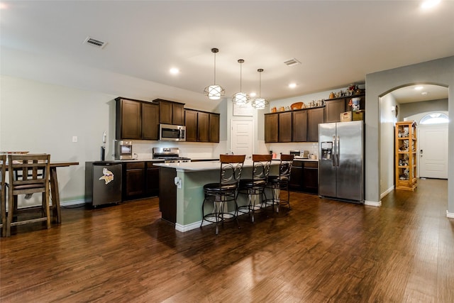 kitchen featuring a kitchen bar, stainless steel appliances, dark brown cabinets, hanging light fixtures, and a center island